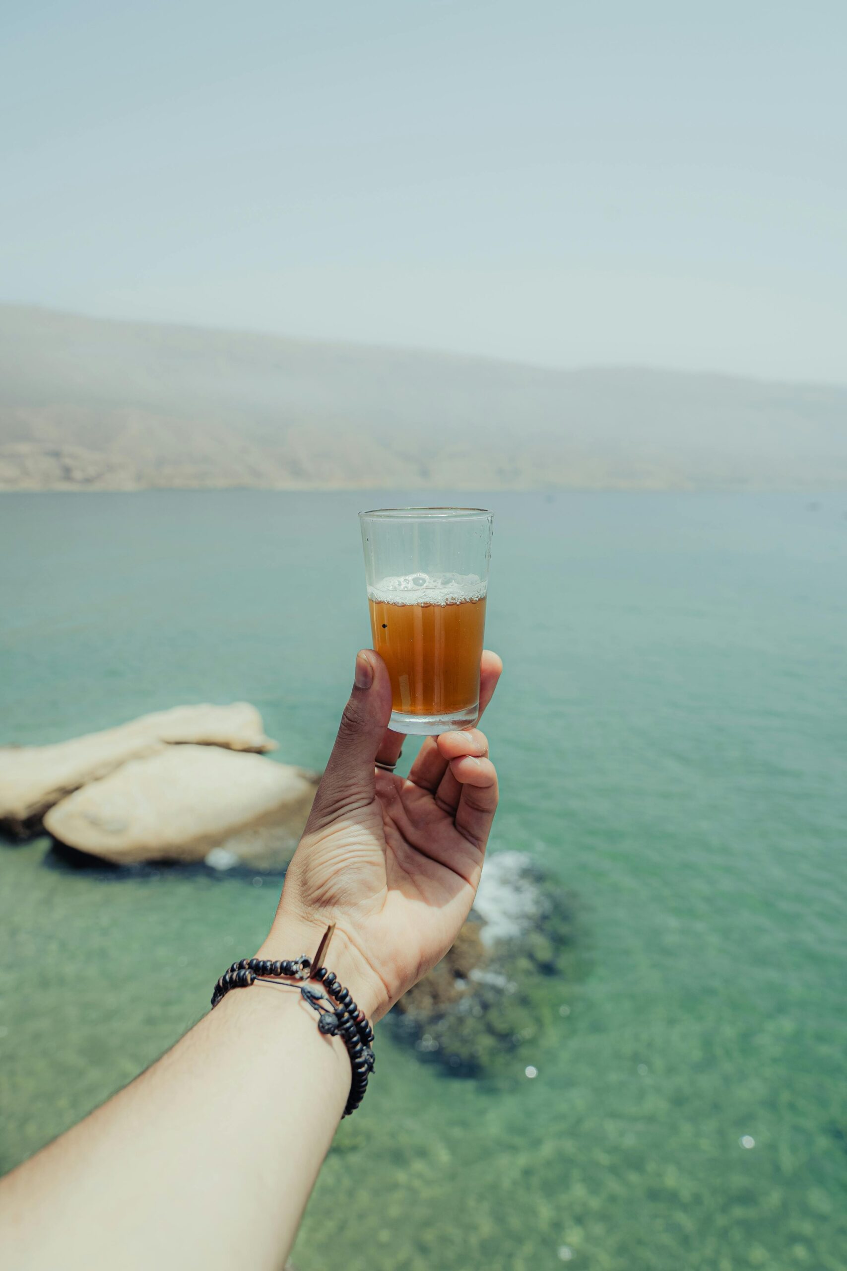 Hand holding a drink against the serene ocean backdrop of Imsouane, Morocco.
